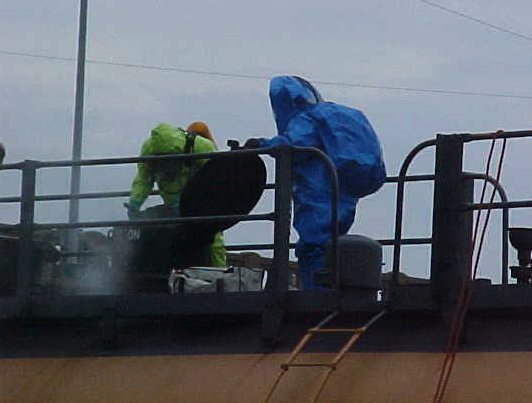 Fire fighters learning how to diffuse a dangerous rail car, while wearing HazMat suits.